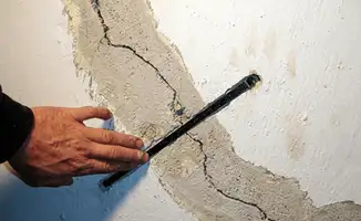 A wall with a large crack is being inspected by a professional in Santa Ana, CA